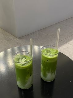 two glasses filled with green liquid sitting on top of a black table next to each other