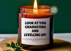 a candle with the words looking at you graduating and leveling up on it next to a plant