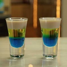 two shot glasses filled with colored liquids on a table