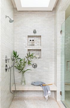 a white tiled bathroom with a plant in the bathtub and shelves on the wall