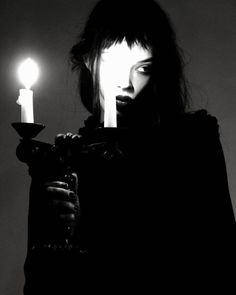 a woman holding two candles in one hand and looking at the camera with an evil look on her face