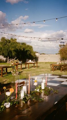 a table with candles and flowers on it in the middle of an outdoor area that has lights strung above