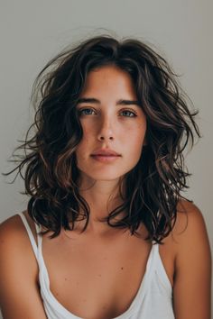 Young woman with shoulder-length wavy hair and a white tank top looking at the camera against a neutral background. Mid Bob Curly Hair, Long Layered Hair Shoulder Length, Mid Length Hair Curly Natural, Wavy Mid Length Hair Styles, Long Bob Curly Haircuts, Medium Length Hair For Wavy Hair, Women Wavy Haircut, Female Shoulder Length Haircut, Curly Waves Short Hair