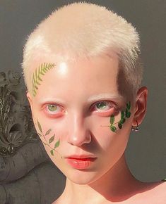 a woman with green leaves painted on her face and chest, standing in front of a statue