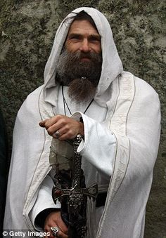 a man dressed in white holding a cross and looking at the camera with his eyes closed