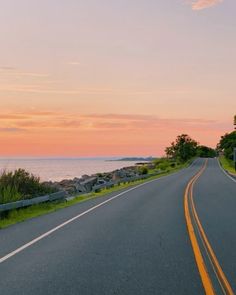 an empty road next to the ocean at sunset