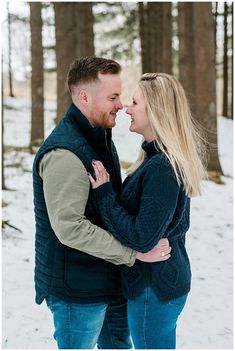 a man and woman standing in the snow with their arms around each other as they look into each others eyes