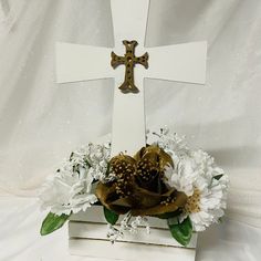 a wooden cross with flowers in it on top of a white cloth covered tablecloth