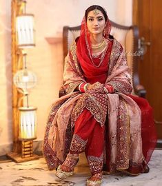 a woman sitting on top of a bed wearing a red and pink dress with gold jewelry