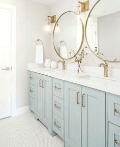 a bathroom with two round mirrors above the sinks and blue cabinetry, along with white towels