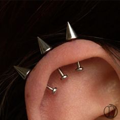 three metal spikes are attached to the side of a woman's ear, with two smaller ones behind them