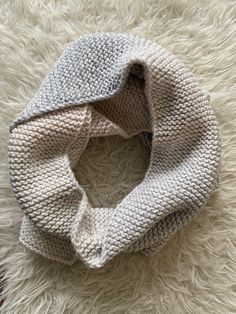 a white and gray knitted scarf on top of a furry rug with a knot in the middle