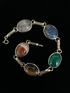 Antique Art Deco 14k Gold Multi-Gemstone Carved Scarab Bracelet 7.5"  Item here is an antique Art Deco 14k gold multi-gemstone carved scarab bracelet. This bracelet features stones such as sardonyx, tiger's eye, chalcedony, lapis, and quartz. Bracelet is marked 14k gold and closes with a spring ring.  Condition: Good; item is pre-owned and may have some signs of light use and age related wear. Please look closely at the pictures provided as they are an extension of our written description. Measurements: Length: 7.5 in Width: .5 in Weight: 8.4 dwt 8731F Antique Multi-stone Bracelet For Formal Occasions, Antique Multi-stone Bracelets For Formal Occasions, Vintage Oval Multi-stone Bracelets, Antique Multi-stone Bracelet As Gift, Antique Multi-stone Bracelets As Gift, Heirloom Multi-stone Bracelets For Formal Occasions, Antique Oval Gemstone Bracelets, Vintage Gold Cabochon Gemstones, Antique Round Gemstone Bracelets