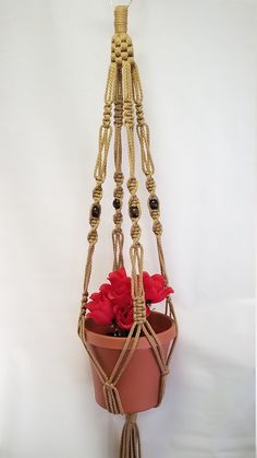 a potted plant hanging from a rope with red flowers in the center and black beads attached to it