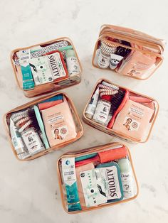 four clear containers filled with personal care items on a white marble counter top, one containing toothbrushes and the other containing toiletries