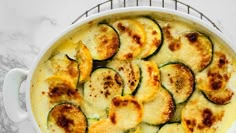 a casserole dish with zucchini and cheese in it on a marble surface