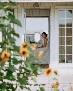 a woman in a wedding dress is sitting on the porch with sunflowers around her