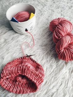 two skeins of yarn next to a ball of yarn and a knitting needle