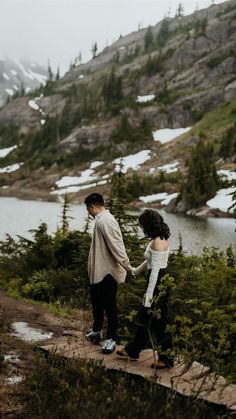 a man and woman standing next to each other on a trail near a body of water