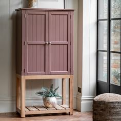 a pink cabinet sitting next to a window in a room with wooden floors and walls