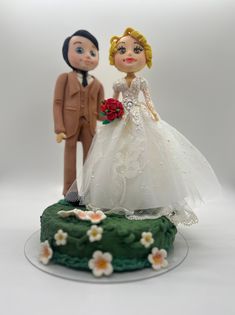 a bride and groom figurine on top of a green cake with white flowers