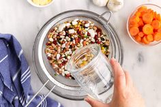 a person holding a glass jar filled with food next to bowls of carrots and other vegetables