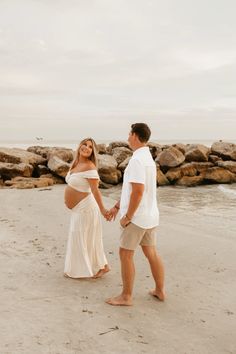 a pregnant couple holding hands on the beach