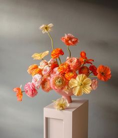 a vase filled with flowers on top of a white table next to a gray wall