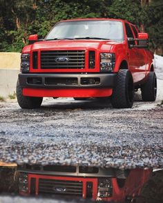 a red truck parked on top of a road next to a puddle filled with water