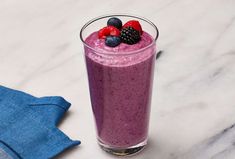 a smoothie with berries and blueberries in a glass on a marble counter top