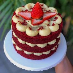 a red velvet cake with white frosting and strawberries on top, sitting on a plate