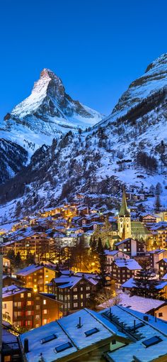 a snowy mountain is in the background with buildings and lights on it, as well as snow - capped mountains