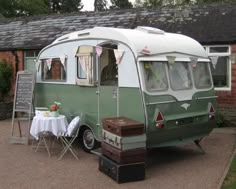 an old camper is parked in front of a house with a table and chairs