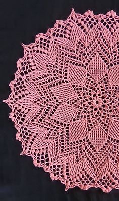 a crocheted doily is shown on a black tablecloth with pink yarn