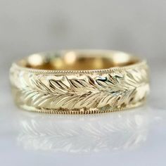 a gold wedding band with leaves on the inside and outside, sitting on a white surface