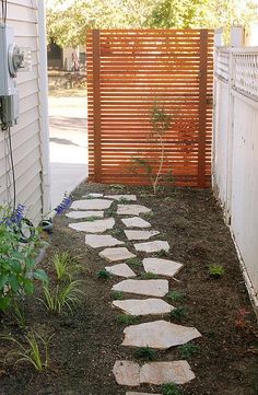 a small garden with stepping stones in the ground and a wooden fence behind it that is next to a house