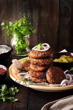 several burgers stacked on top of each other with onions and green sauce in the background