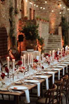 a long table is set up with white and red flowers, candles and place settings