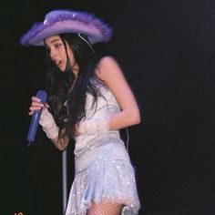 a woman in a white dress and purple hat holding a blue microphone while standing on stage