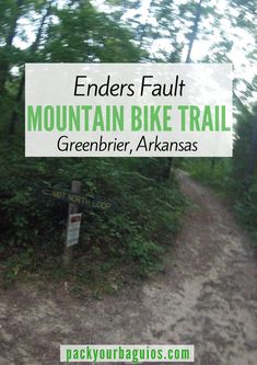 a trail sign on the side of a dirt road with trees and bushes in the background