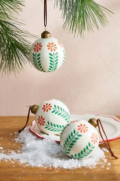 three ornaments hanging from a pine tree on top of snow covered plates and saucers