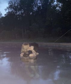 two people are kissing in the middle of a body of water with trees in the background