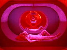 a woman laying on top of a bed in a room with red and purple lights