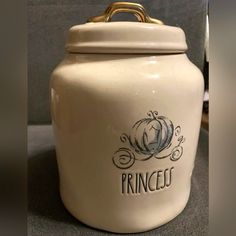 a white ceramic jar with the word princess on it and a gold handle is shown