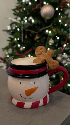 a snowman mug with a gingerbread cookie in it's mouth next to a christmas tree