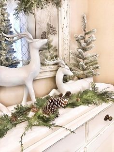 a white mantle decorated with pine cones, evergreen and deer figurines