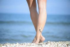 a woman's legs with a tattoo on the beach