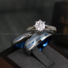 two wedding rings are sitting on top of each other in a wooden box with blue and white bands