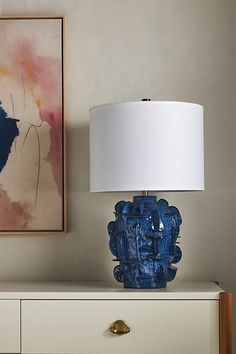 a blue vase sitting on top of a white dresser next to a painting and lamp