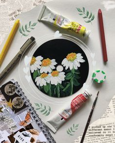 a plate with daisies painted on it next to paintbrushes and other art supplies